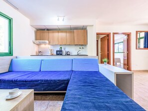 A modern living room with a sofa, a small table, and a kitchen area with wooden cabinets and a microwave. - Festival Village by Interhome (Salou)