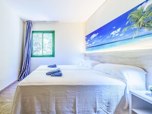 A hotel room with a bed, a window with curtains, a wall mural of a beach, and a nightstand with a plant. - Festival Village by Interhome (Salou)