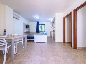 A modern room with a dining table, chairs, a sofa, a TV, and a kitchen area. - Festival Village by Interhome (Salou)