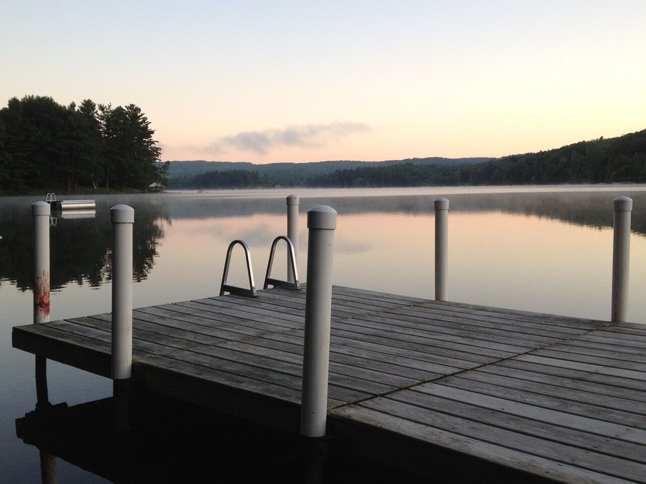 A wooden dock extending into calm water with metal bollards and a metal ladder.
