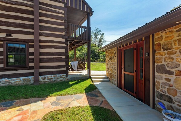 A log cabin with a stone exterior, a covered porch, and a stone pathway leading to the entrance.