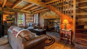 Ein rustikaler Blockhaushof mit einer Holztreppe, einem Kamin, einem Ledersofa und einem Essbereich.