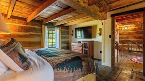 Ein Schlafzimmer in einer Blockhütte mit Bett, Kommode und einem an der Wand befestigten Fernseher.