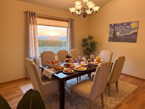 A dining area with a table set for breakfast, a chandelier, and a painting on the wall.
