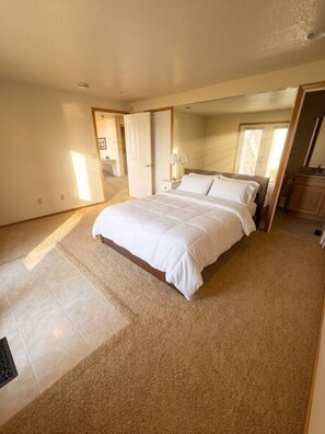 A bedroom with a large bed, a nightstand, a mirror, and a door leading to another room.