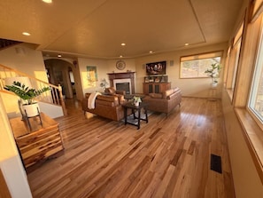 A spacious living room with a fireplace, wooden flooring, and a large window.