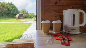 Een houten interieur met uitzicht op een groen landschap, een klein houten gebouwtje en een witte elektrische waterkoker op tafel.