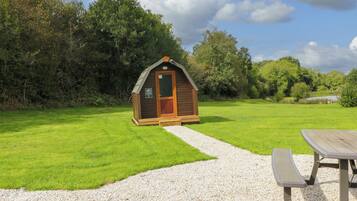 Een klein houten huisje met een grindpad er naartoe, omgeven door weelderige begroeiing.