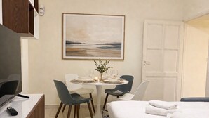 Een hotelkamer met een bed, een bureau met televisie, een kleine tafel met stoelen, een schilderij aan de muur en een deur.
