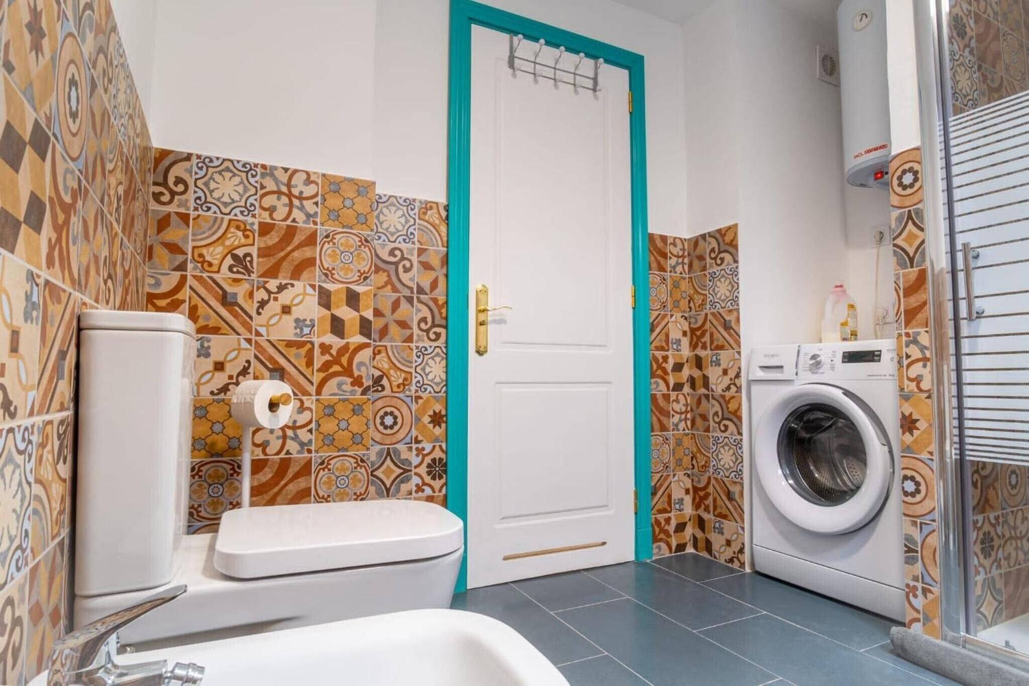 Une salle de bain avec des carreaux décorés, des toilettes, un lavabo et un lave-linge.