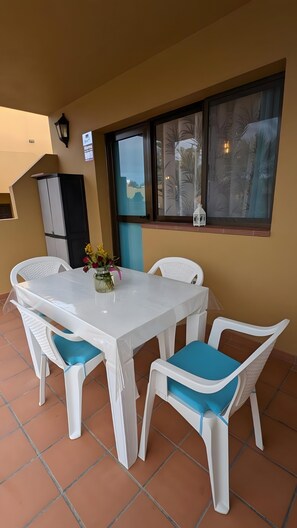 Un comedor con una mesa y sillas blancas, un florero con flores y un ventanal con vistas.