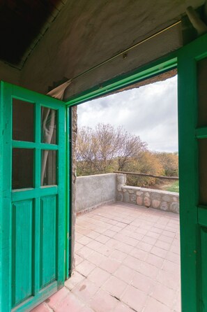 Una habitació amb una porta verda i vista a un balcó amb mur de pedra i arbres.