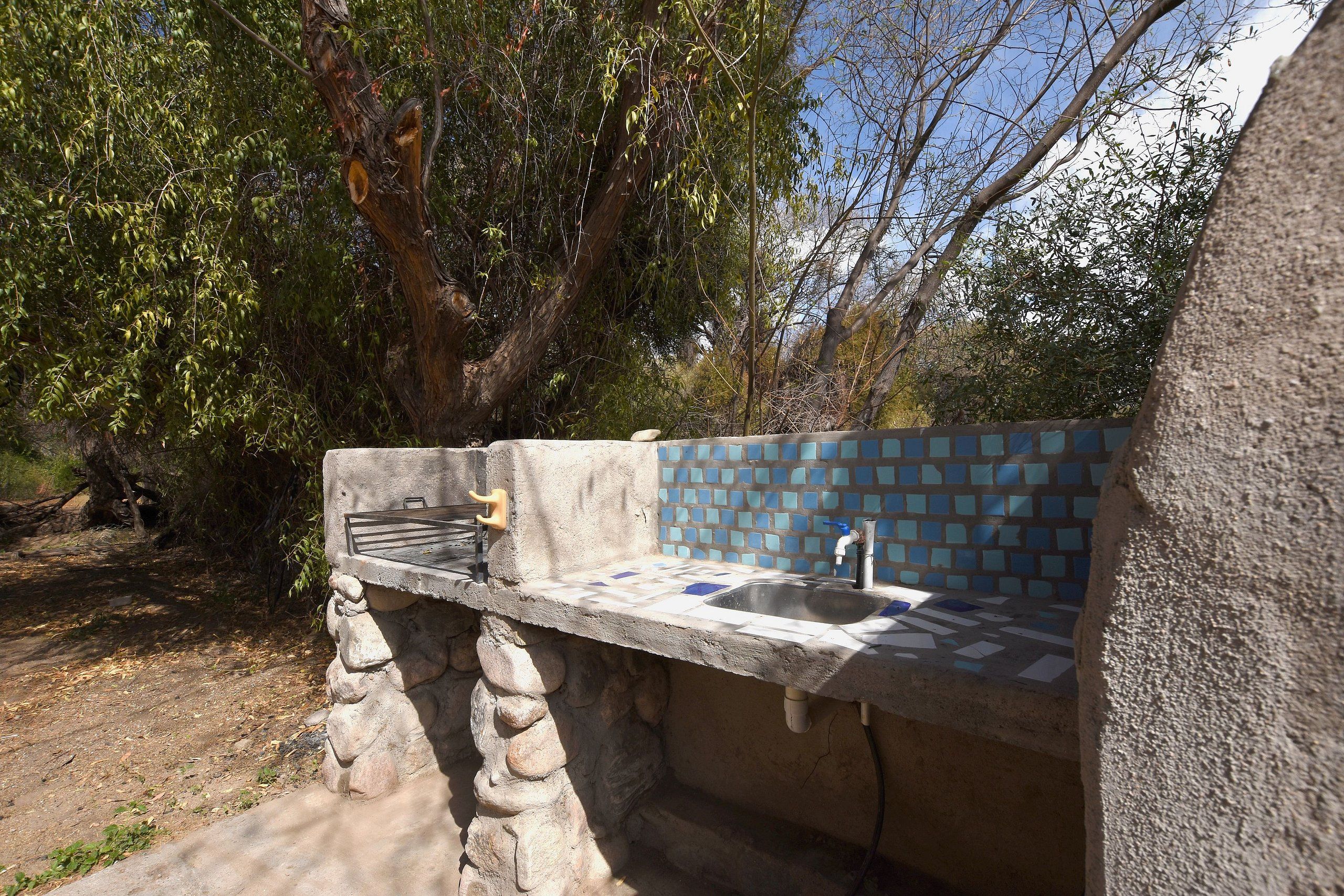 Una zona de cocina exterior con un lavabo de piedra y una parrilla.