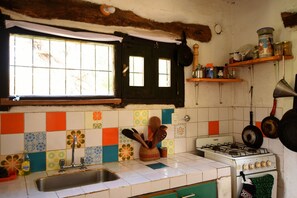 Una cocina con estufa a gas, un lavamanos y un ventanal con cortinas.
