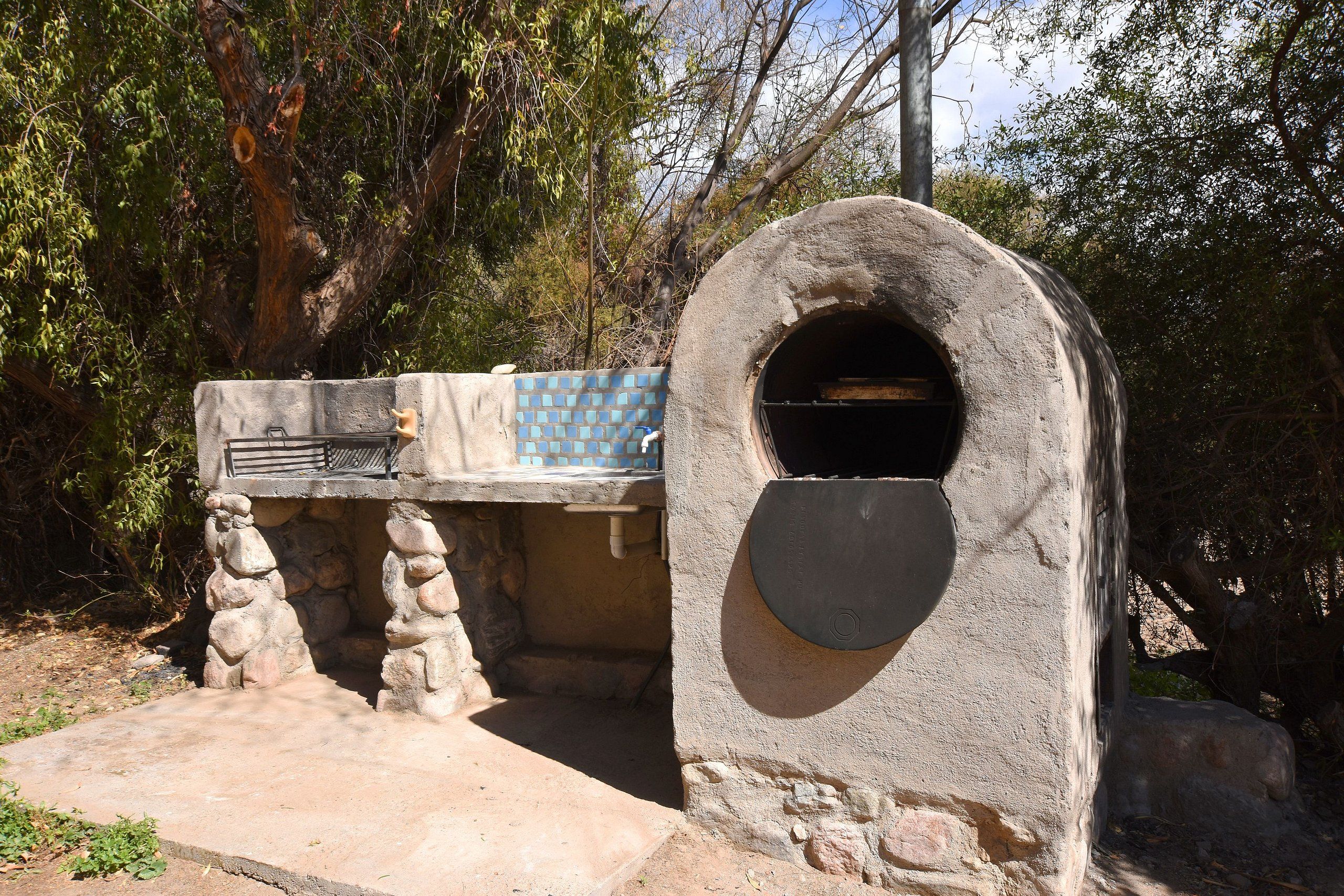 A stone-built outdoor kitchen with a built-in oven, surrounded by trees.