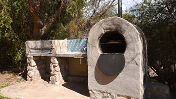 A stone-built outdoor kitchen with a built-in oven, surrounded by trees.