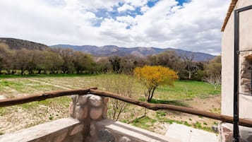 A stone structure with a metal railing, overlooking a grassy field with trees and mountains in the distance.