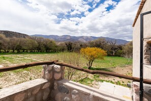 Una estructura de piedra con barandilla metálica, que domina un campo cubierto de hierba con árboles y montañas al fondo.