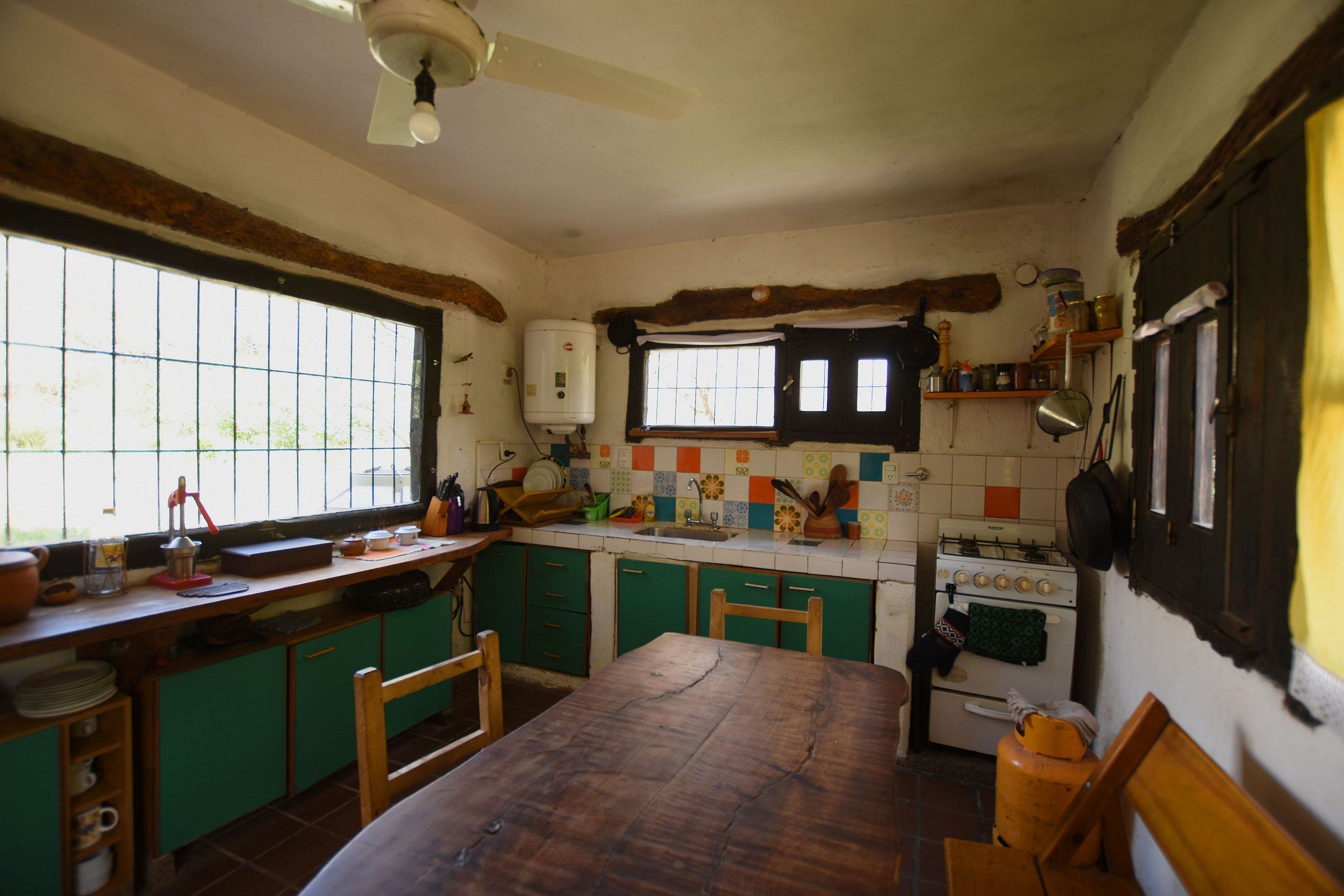 A kitchen with a wooden table, green cabinets, a stove, and a window with bars.