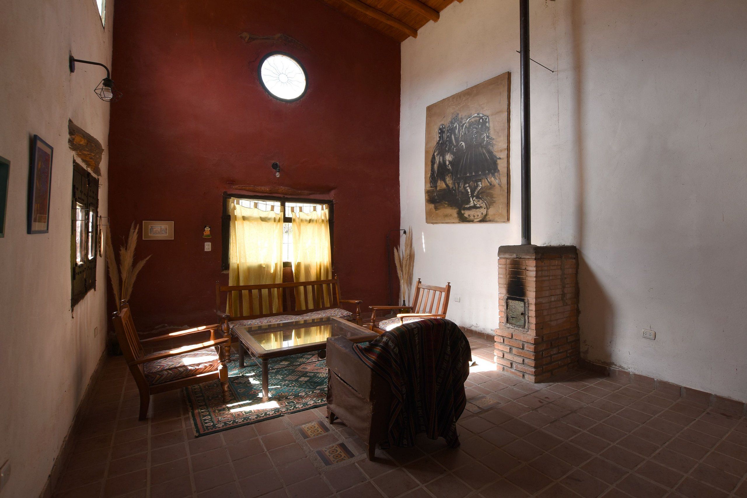 A room with a red wall, a wooden bench, a table, a patterned rug, a fireplace, and a painting.
