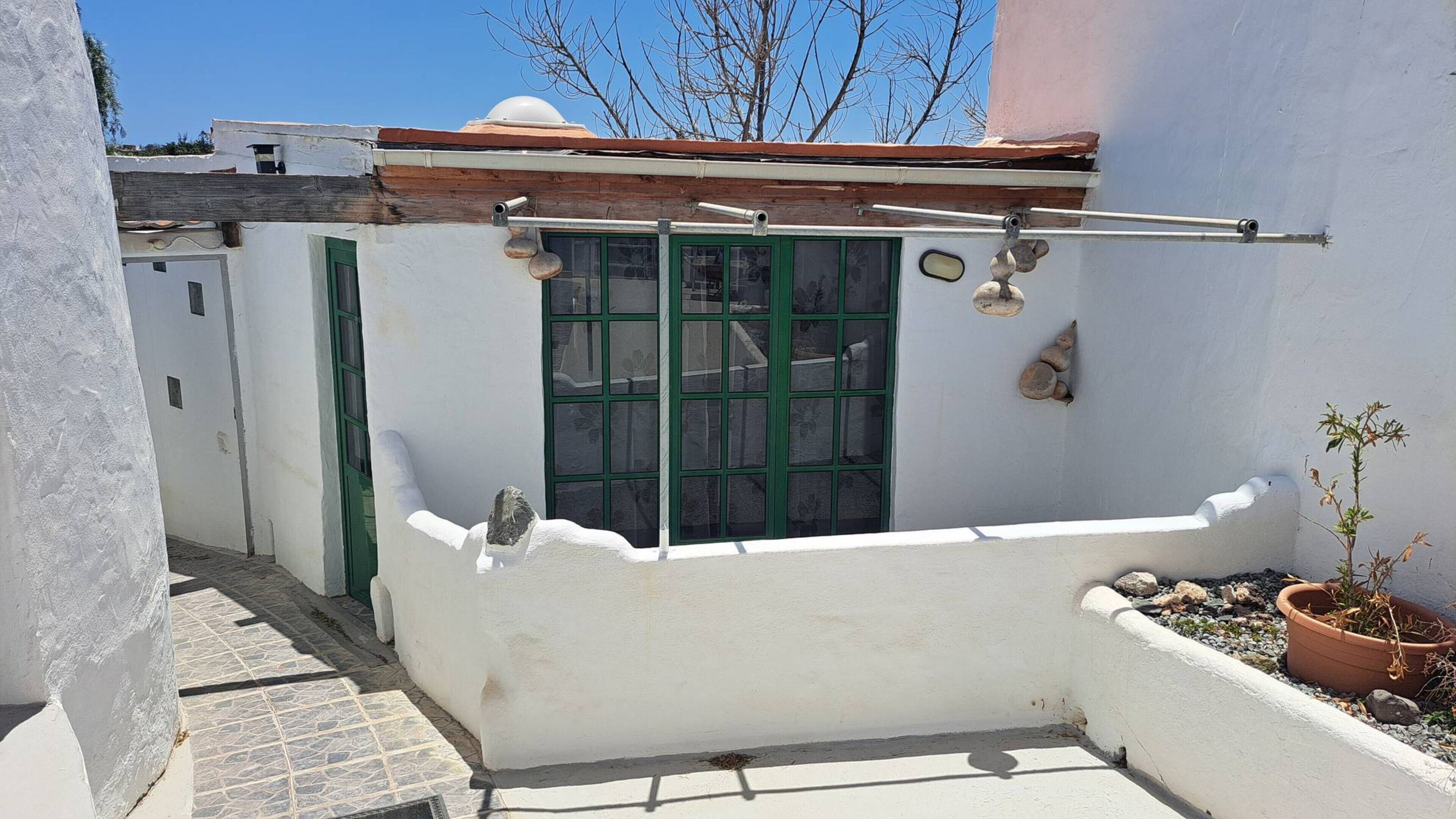 A white-walled building with a green door, a window with a metal grill, and a small potted plant.