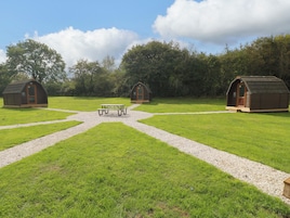 Un camping con tres cabañas de madera, una mesa de picnic y senderos de grava.