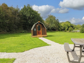 A small wooden cabin with a gravel path leading to it, surrounded by lush greenery.