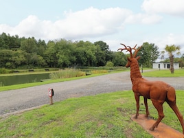 A deer statue on a gravel path with a speed limit sign, surrounded by greenery and a body of water.