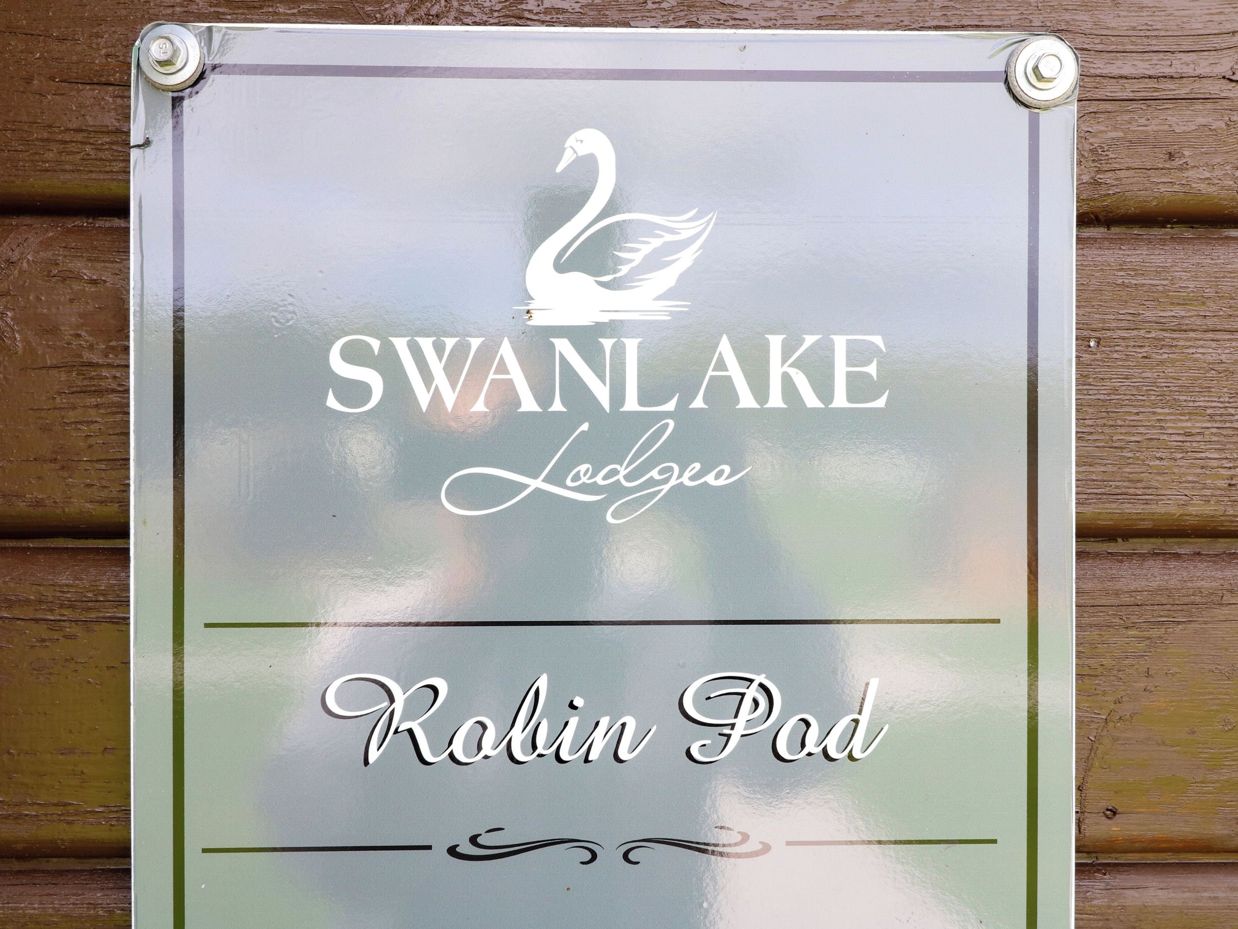 Une enseigne portant l’inscription « SWANLAKE Lodges Robin Pod » et le logo d’un cygne.