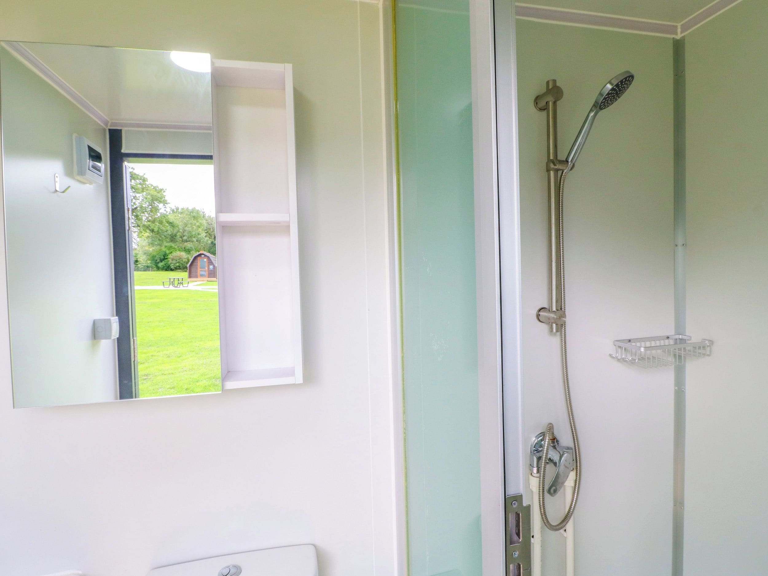 A bathroom with a shower, a mirror, and a view of a green lawn and building outside.