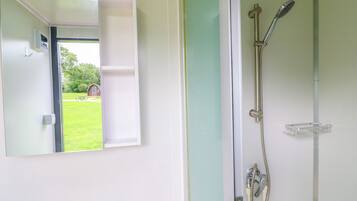 A bathroom with a shower, a mirror, and a view of a green lawn and building outside.
