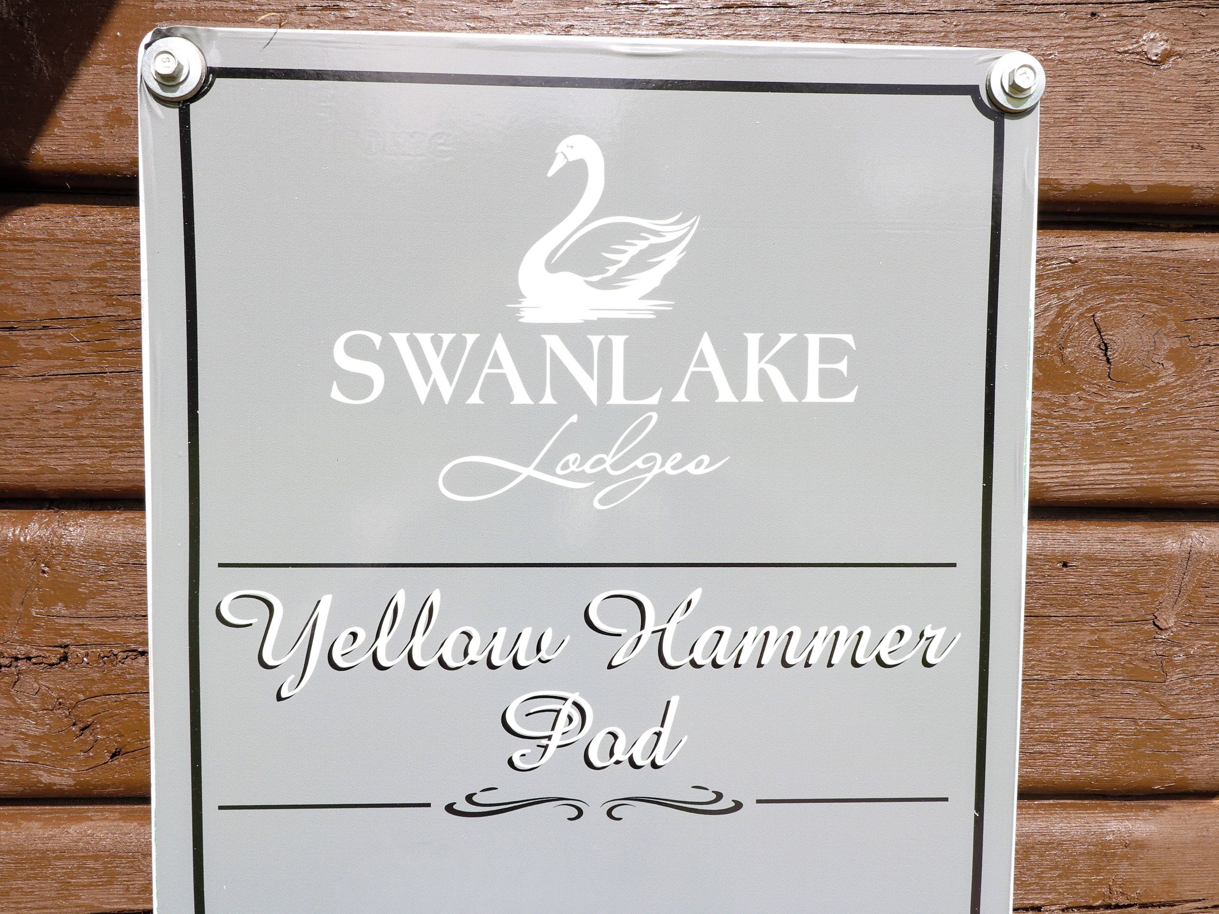 Un letrero muestra el texto 'SWAN LAKE Lodge' y 'Yellow Hammer Pod' sobre un fondo de madera.