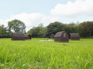 Una hilera de pequeñas cabañas de madera en un campo cubierto de césped, con una mesa de picnic en el centro.