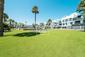 A modern building with a flat roof, large windows, and a well-maintained lawn with palm trees. - Oasis Beach Sunscape Penthouse, Private rooftop and resort wellness by OYOOSTAYS (Guardamar del Segura)