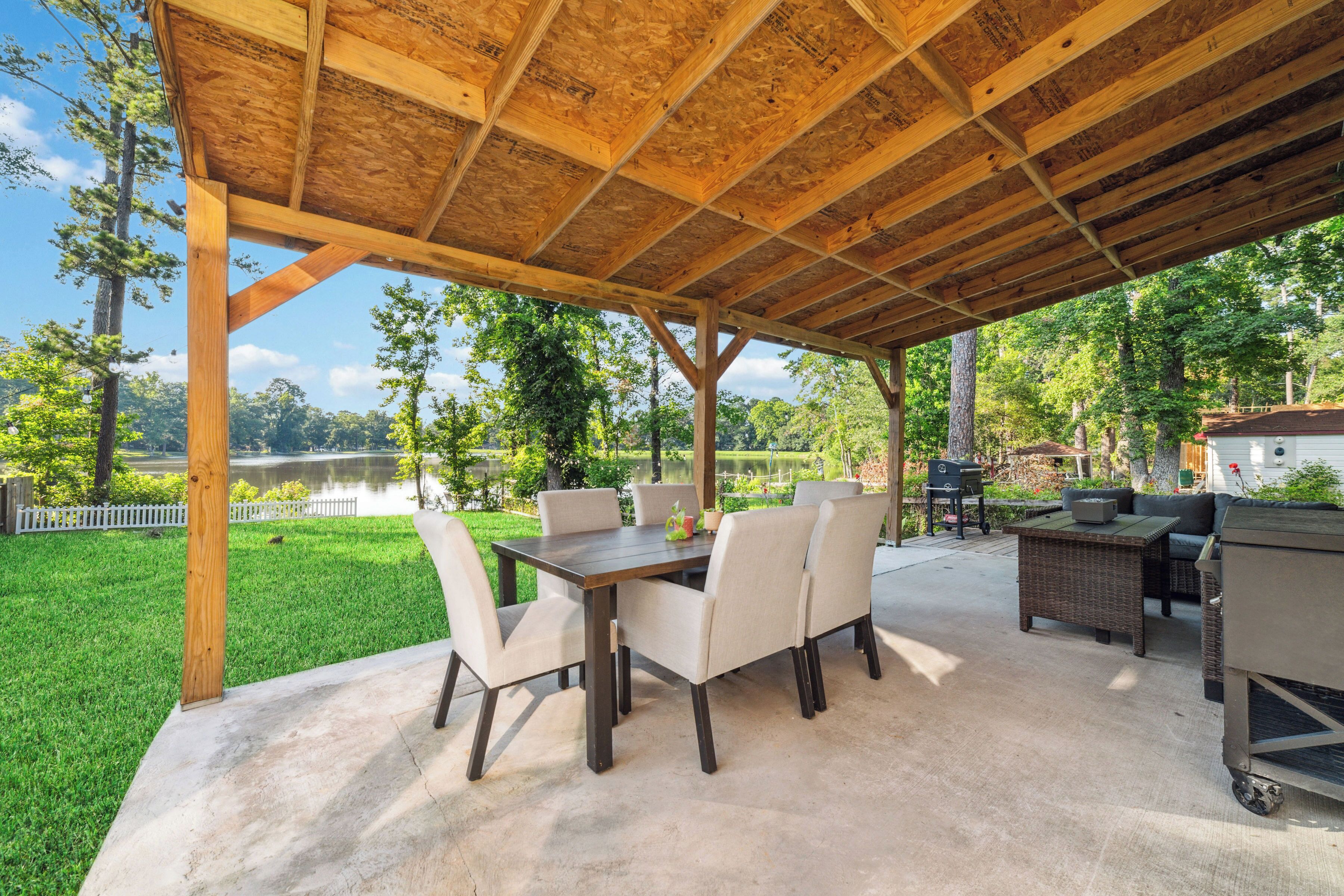 Une terrasse couverte avec une table et des chaises, un barbecue et une vue sur un lac.