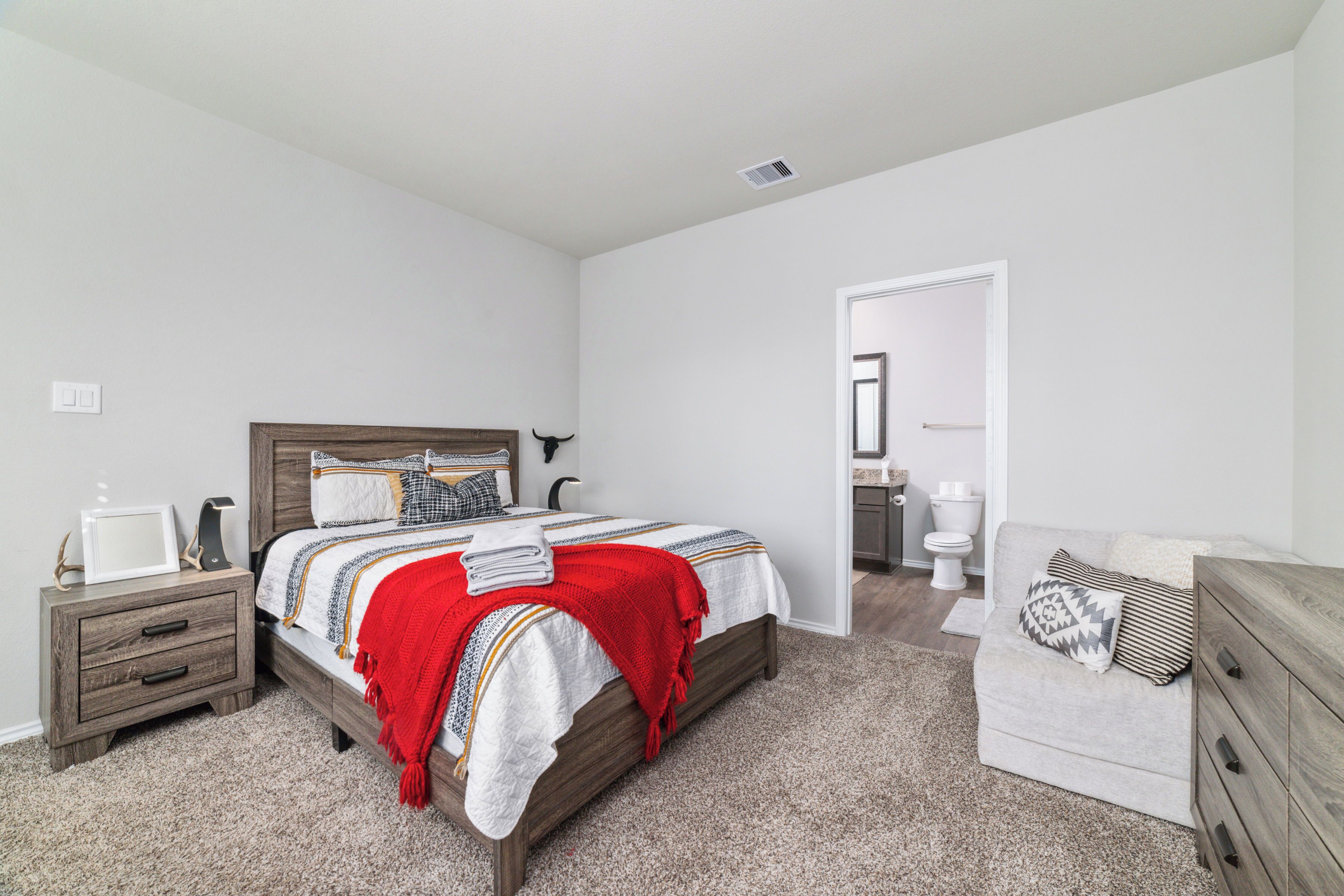 A bedroom with a bed, nightstand, dresser, and a bathroom visible through an open door.