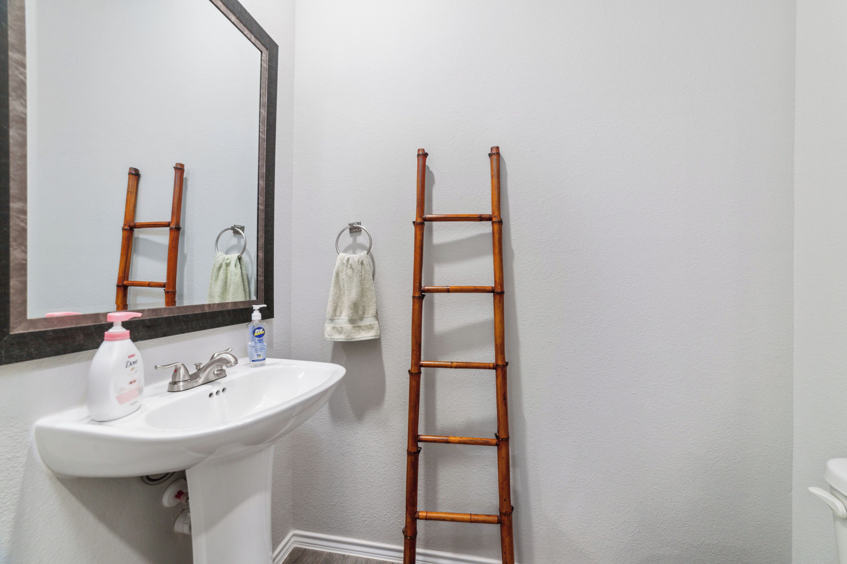 A bathroom with a white sink, mirror, and a wooden ladder leaning against the wall.