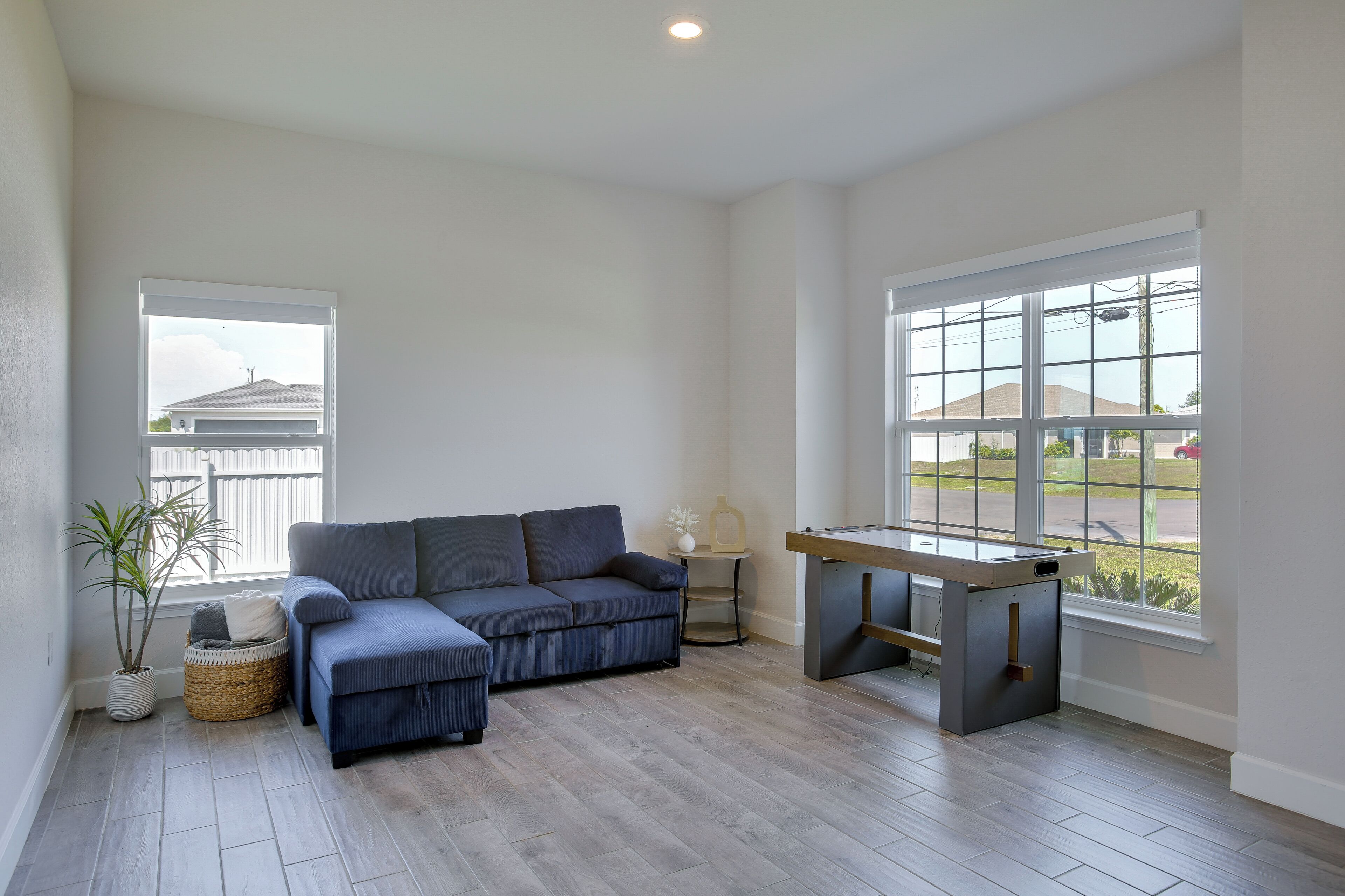 A room with a grey sofa, a wooden table, a window with a view, and a plant.