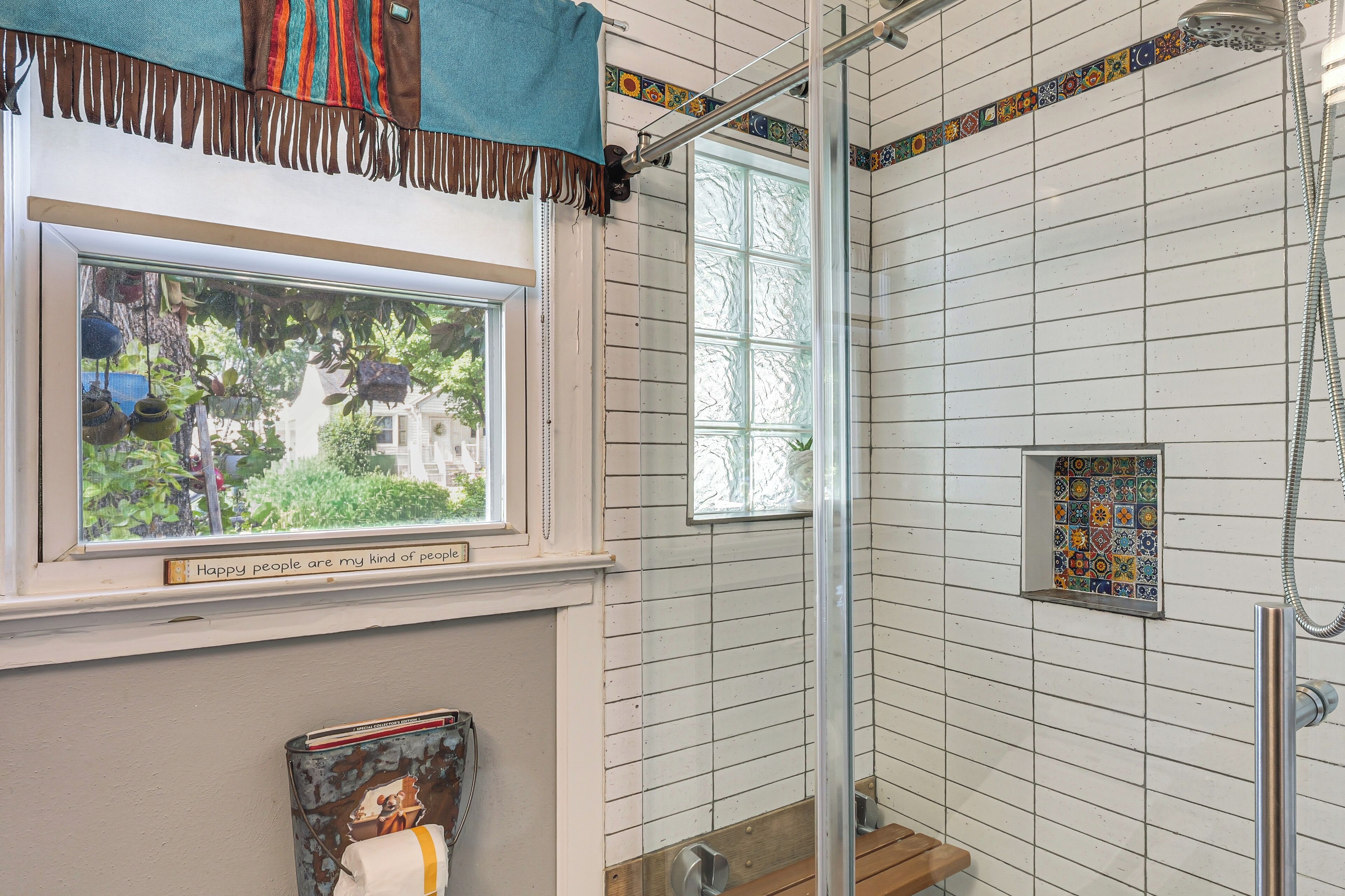 A bathroom with a shower, a window with a view, and a decorative tile border.