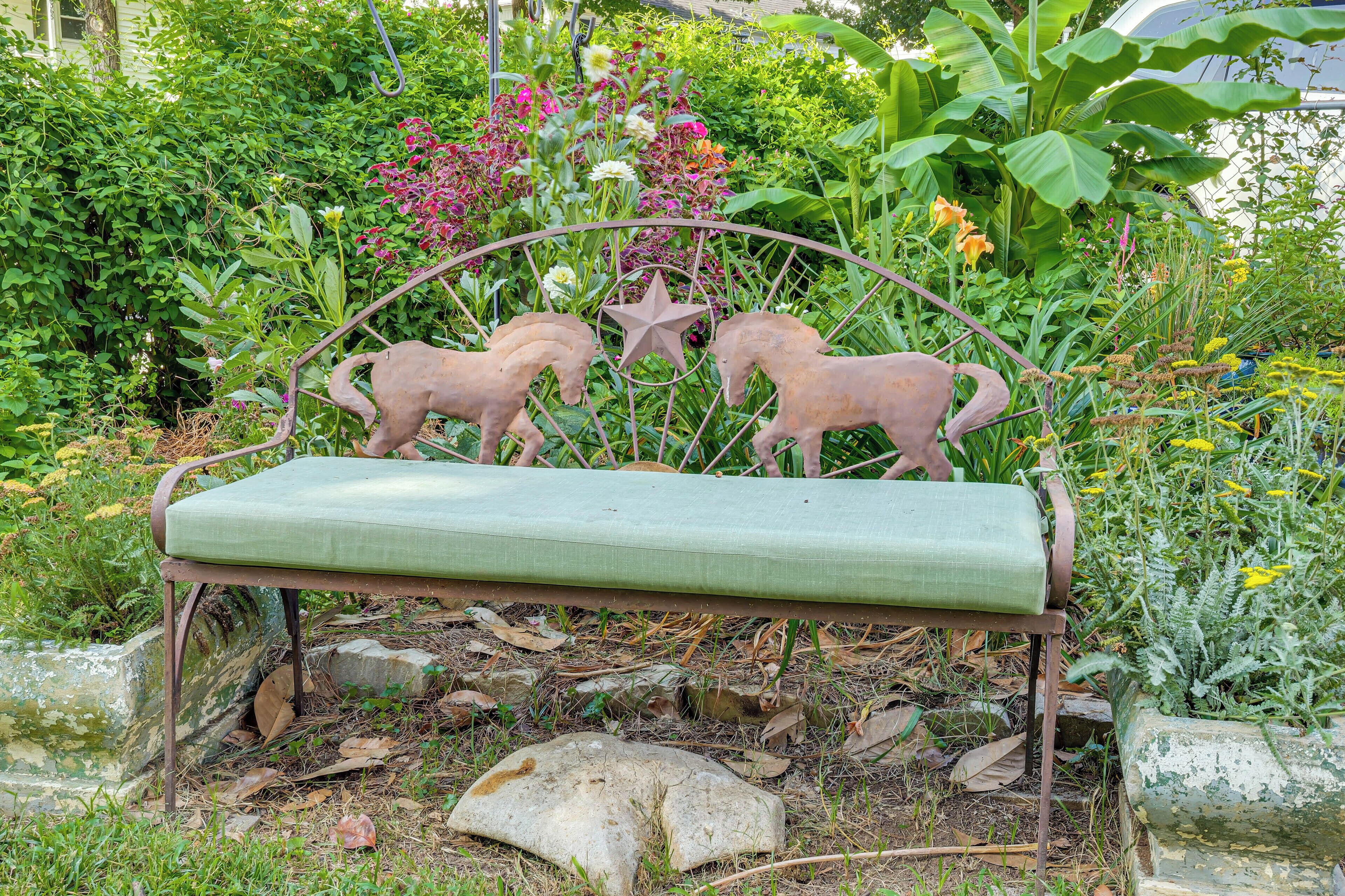A metal bench with a green cushion in a garden with various plants and a star decoration.