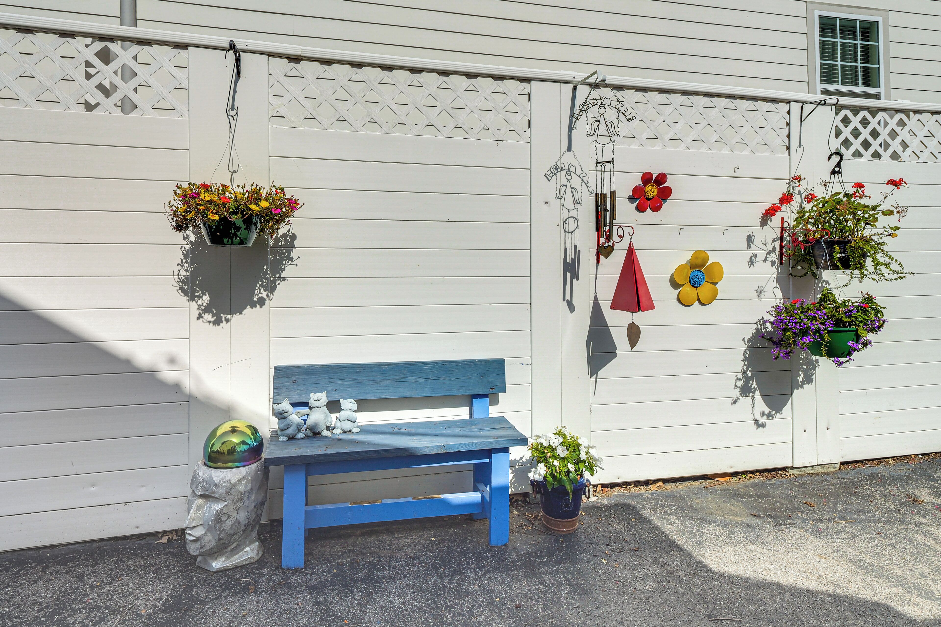 A blue bench, white fence, and hanging flower pots.