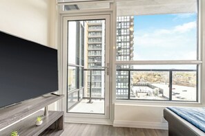 A modern apartment with a balcony, a TV, and a view of a high-rise building.