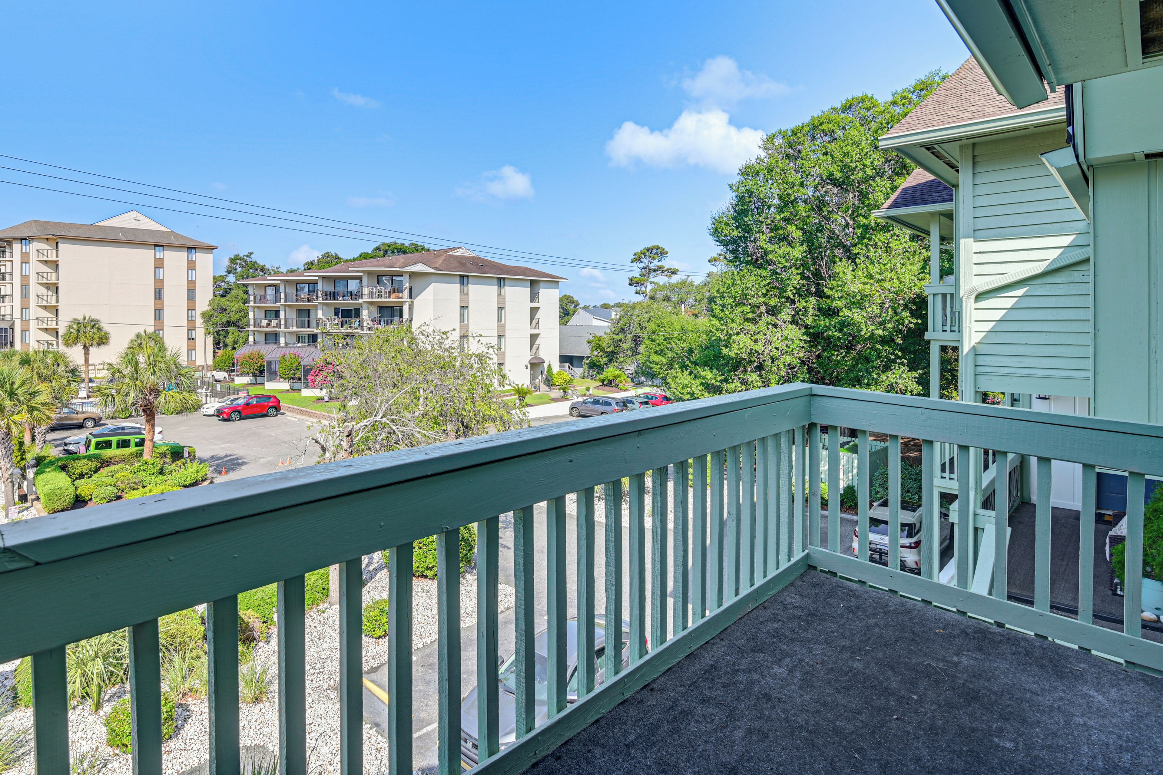 A balcony with a view of a parking lot, buildings, and trees.