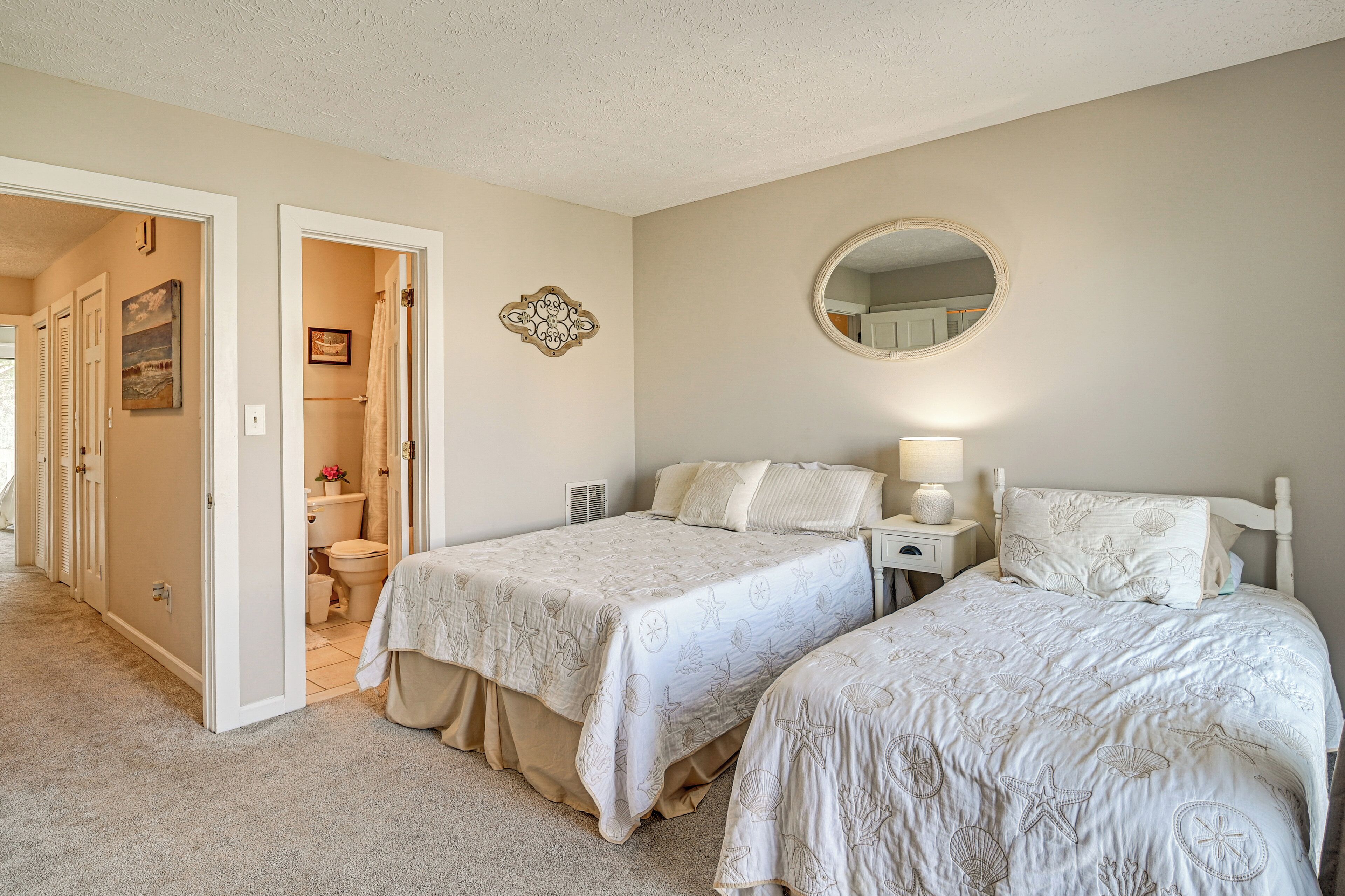 A bedroom with two beds, a bathroom, and a hallway.