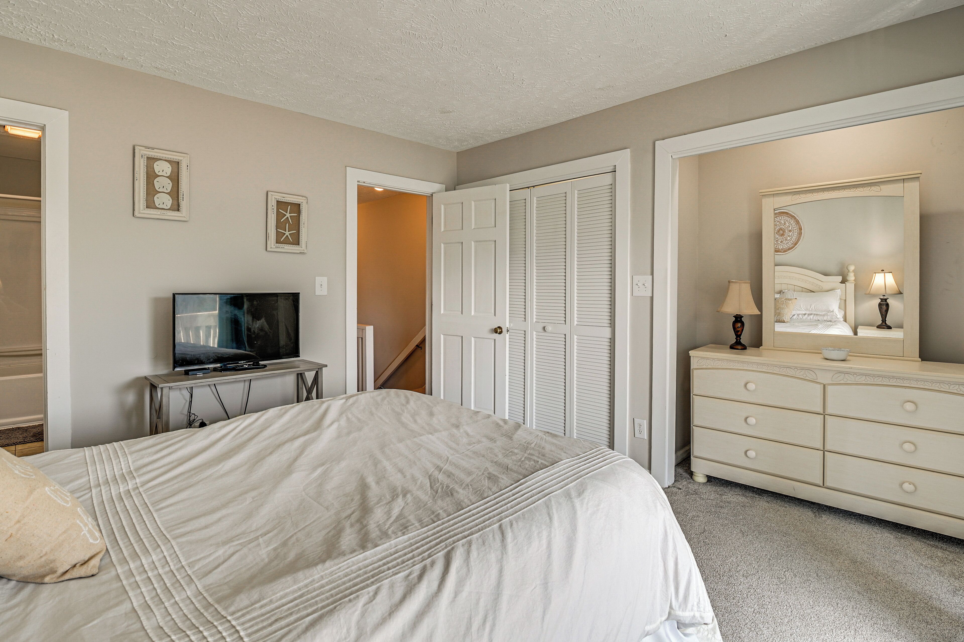 A bedroom with a bed, dresser, television, and a door leading to another room.