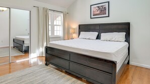 Un dormitorio con cama, mesita de noche, lámpara, ventana con cortinas y un cuadro en la pared.
