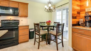 Una cocina con armarios de madera, una estufa negra, una mesa de comedor con sillas y una zona para café.