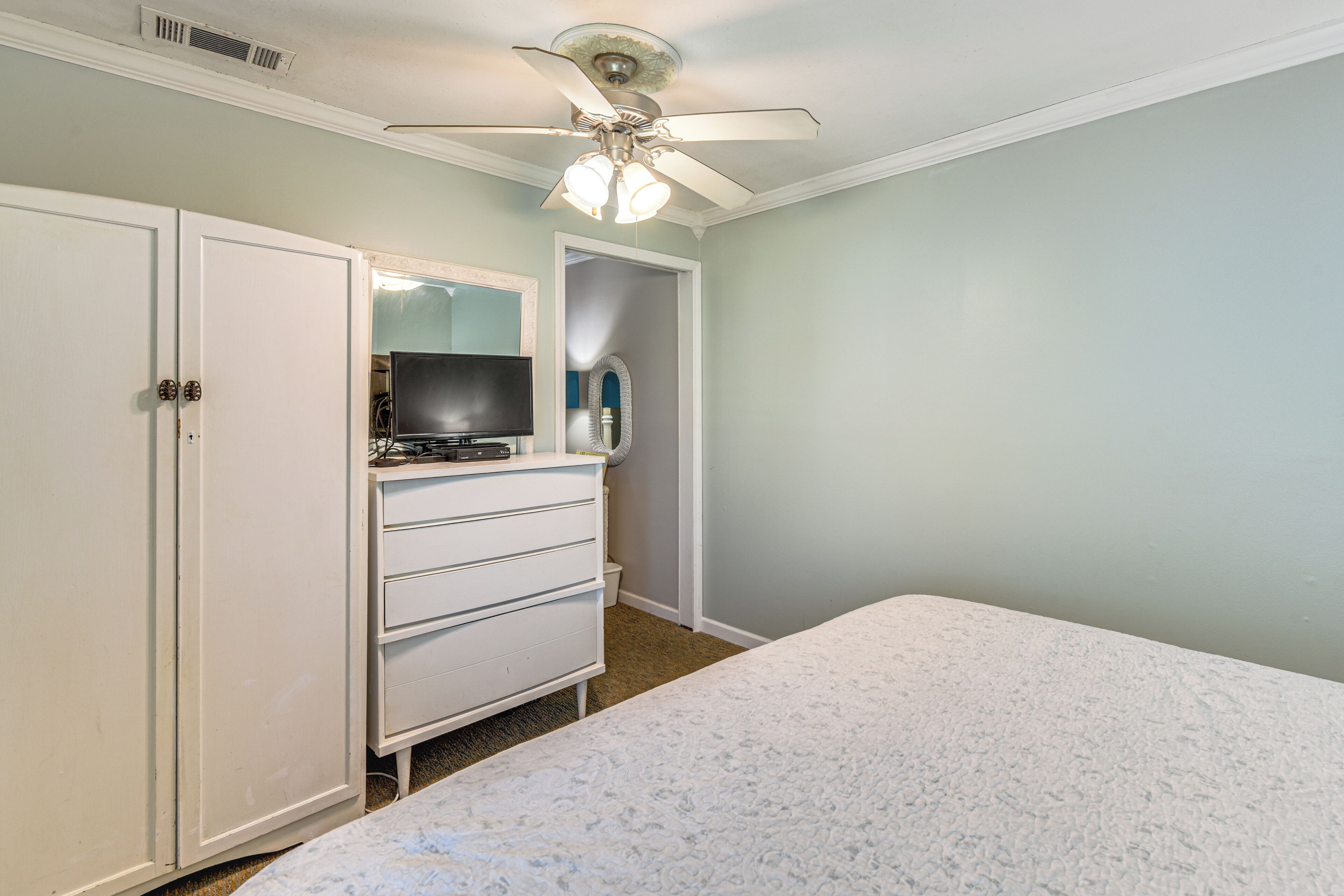 A bedroom with a bed, a dresser, a television, and a ceiling fan.