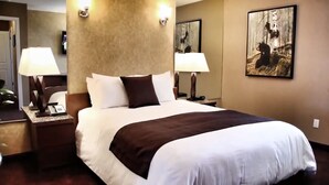 Une chambre d’hôtel avec un grand lit, deux lampes de chevet, une table de chevet, un téléviseur fixé au mur et un tableau encadré.