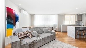 Ett modernt vardagsrum med en grå soffa, en stor abstrakt målning och en köksdel med en bänkskiva i marmor.